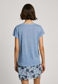 Gaiši zils, īsām piedurknēm T-krekls ar apaļu kakla izgriezumu; mīksta struktūra. Kombinēts ar ziedu raksta svārkiem, kuros ir zili un tumši ziedi.