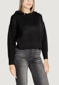 Felpa cropped nera in tessuto a maglia, con una vestibilità comoda, orlo a coste e maniche lunghe. Abbinata a jeans grigi.