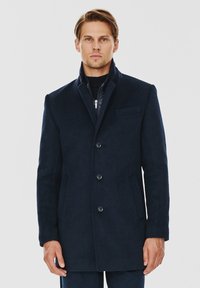Granatowy wełniany płaszcz o dopasowanym kroju, z wyciętym kołnierzem, zapięciem na guziki, dwoma bocznymi kieszeniami i teksturowanym materiałem.