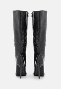 Bottes noires en cuir synthétique montant jusqu'au genou, avec une texture crocodile, un bout pointu et un talon aiguille. Elles disposent d'une fermeture éclair à l'arrière.