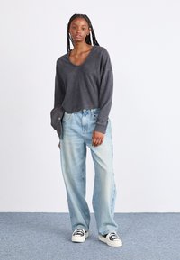 Haut gris à manches longues avec un large décolleté, associé à un jean ample bleu clair et des baskets noir et blanc. Texture de tissu lisse.