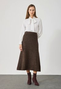 Witte blouse met strikkraag, gecombineerd met een bruine wollen A-lijn rok en bordeauxrode enkellaarzen. Gladde stof en getailleerde pasvorm.