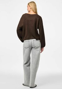 Brūns, lielā izmēra adīts džemperis ar plašu kakla izgriezumu. Kombinēts ar gaismas pelēka, augsto jostasvietu, taisnu kāju džinsiem. Gluda tekstūra un brīva piegriezuma.