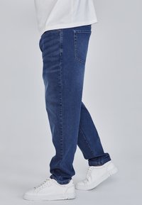 Tumesinised sirge lõikega teksad, millel on õmblused ja kaks tagataskut, kantud koos valgete tossudega. Sile teksakangas.