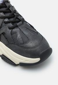 Mustad sneaker, mille, mis sisaldab võrgupaneele ja tekstureeritud sünteetilist materjali, koos valge vaheosaga ja kummist välispõhjaga. Paelad ja pehmendatud keel on kaasas.