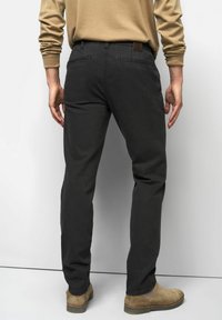 Zwarte stretchkatoenen broek met een slim fit, achterzakken en een bruine leren patch op de taille. Gecombineerd met beige suède enkellaarsjes.