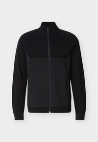 Veste noire zippée intégrale avec col, poignets et ourlet côtelés, dotée de poches latérales zippées et d'un panneau texturé sur le haut de la poitrine.