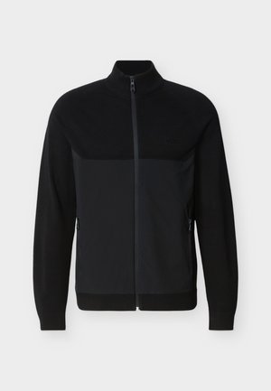 Čierna bunda na celkové zapínanie na zips s rebrovaným golierom, manžetami a lemom, vybavená bočnými vreckami na zips a textúrovaným panelom na hornej časti hrudníka.