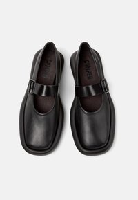 Zapatos Mary Jane de cuero negro con punta cuadrada, suela plana y correa ajustable en el empeine. Forro interior suave visible.