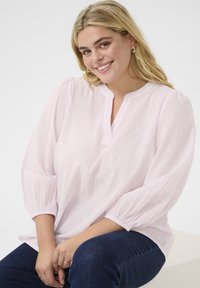 Helles rosa Blusenshirt aus strukturiertem Stoff mit 3/4 Puffärmeln und rundem Ausschnitt. Kombiniert mit dunkelblauen Jeans.