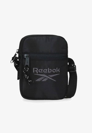 Bolso bandolera compacto negro con bolsillo frontal con cremallera, correa ajustable y logo gris de Reebok en el panel frontal.