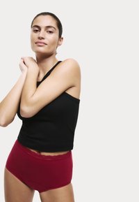 Un débardeur noir côtelé associé à un short taille haute rouge avec une finition en dentelle. Design simple avec une texture lisse.