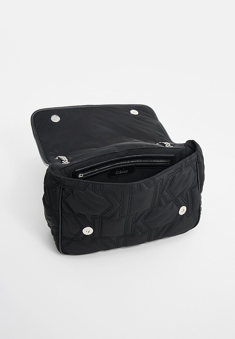 Sac à épaule matelassé noir avec une texture douce, doté d'une poche zippée à l'intérieur et de bouton-pression métalliques sur le dessus.