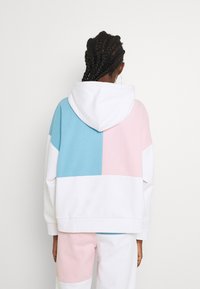 La sudadera con capucha presenta un diseño en bloques de color con secciones en azul, rosa y blanco. Confeccionada en tejido suave, tiene un ajuste relajado y puños acanalados.