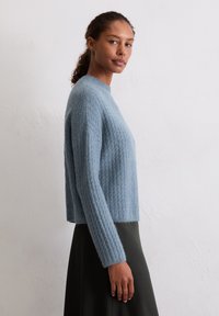 Himmelblauer, strukturiert gestrickter Pullover mit Rundhalsausschnitt und langen Ärmeln, der eine verkürzte Passform und gerippte Bündchen aufweist, kombiniert mit einem dunklen Rock.