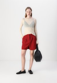 Haut léger à manches longues crème avec une doublure vert menthe, associé à un short rouge taille haute et des mocassins noirs ; tenant un sac noir.
