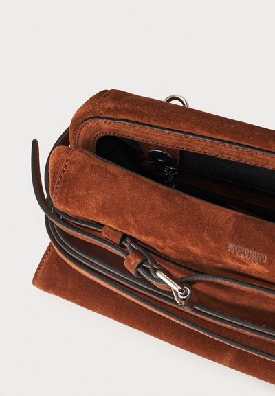 Sac à main Moschino en daim marron avec cordon en cuir noir et fermeture métallique, montré partiellement ouvert sur un fond uni.