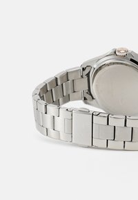 Pulsera de reloj de acero inoxidable plateado con eslabones rectangulares, que presenta una caja de reloj brillante y un acento en oro rosa en la corona. Detalle del logotipo grabado.