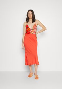 Top vermelho sem mangas com padrão floral e decote profundo em V, combinado com uma saia laranja até ao joelho. Sandálias laranjas com tiras completam o conjunto.