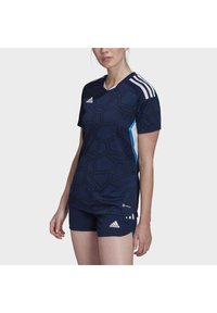 Maglietta sportiva blu navy e pantaloni corti con texture geometrica, caratterizzati da accenti bianchi e blu. Logo del marchio sul petto e sui pantaloni. Maniche corte.