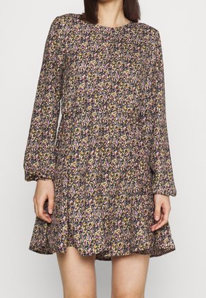 Mujer con un vestido largo de manga larga con estampado floral, escote redondo y falda acampanada sobre un fondo liso.