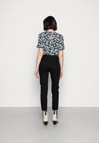 Blusa con stampa floreale e maniche corte, jeans neri a vita alta e stivali alla caviglia beige con accenti neri, visti da dietro.