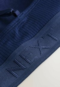 Tissu bleu marine avec une texture côtelée et le logo "NEXT" en relief. Le tissu présente des motifs variés et une finition lisse.