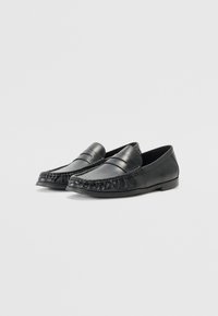 Sorte skinnloafer med en strømlinjeformet design, med søm-detaljering rundt tåen og en glatt overflate, egnet for både uformell og formell bruk.