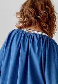 Indumento blu con un design ampio e arricciato. Presenta un collo testurizzato con dettagli in pizzo bianco. Tessuto morbido.