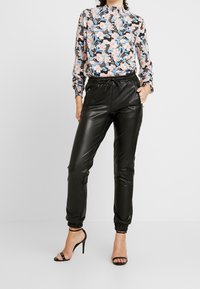 Sorte joggingbukser i kunstlæder med elastiske manchetter, kombineret med en mønstret, pink og sort langærmet bluse med blomsterprint.