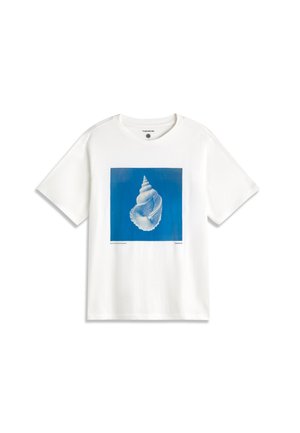 T-shirt blanc à manches courtes avec un grand carré bleu présentant un motif détaillé de coquillage blanc centré sur le devant.