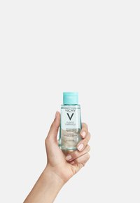 Vichy Pureté Thermale eye makeup remover in a transparent bottle with a light blue cap. 100 ml size. Hand holding the product.