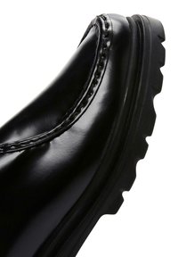 Botín negro de cuero con acabado suave, detalles de costura y suela texturizada para tracción. Forma curva con un diseño elegante.