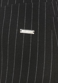 Zwarte stof met verticale witte streepjes, voorzien van een metallic zilverkleurig label met de opdruk "LASCANA". Glad van structuur.