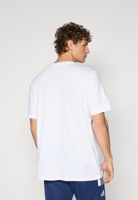 Hvid bomulds t-shirt med rund hals og korte ærmer, der har en løs pasform og et mærke på den nederste side. Enkel og simpel design.