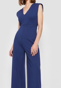 Mono azul marino con un escote en V profundo, mangas cortas, cintura ajustada y pantalones de pierna ancha, confeccionado en una tela suave y elástica.