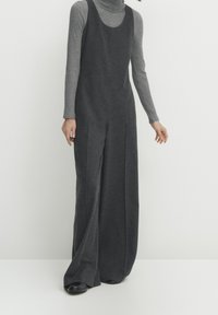 Combinaison gris à jambes larges en tissu doux, avec un décolleté arrondi et des coutures latérales. Portée par-dessus un col roulé gris ajusté.