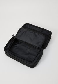 Black nylon zippered tech organizer with dual compartments; one mesh pocket and logo patch. Smooth texture, rectangular shape, lightweight design.