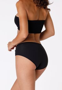 Top bandeau nero senza cuciture e parte inferiore abbinata a vita alta, realizzati in morbido tessuto elasticizzato, con bordi lisci e cuciture minime.