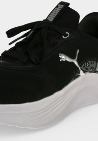 Μαύρο αθλητικό παπούτσι Puma με λευκή σόλα, ασημένιο λογότυπο Puma, μαύρα κορδόνια και λεπτομέρεια με λεοπάρ μοτίβο κοντά στη φτέρνα.