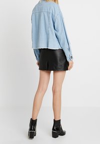 Světle modrá džínová bunda s cropped designem a třepeným lemem, doplněná černou koženou mini sukni a botami na podpatku kotníkového střihu.