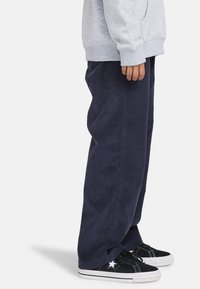 Marineblå kordfløjspant med en afslappet pasform, parret med sorte sneakers med et hvidt stjernedesign og hvide gummisåler.