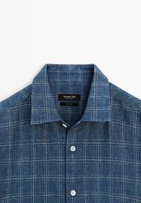 Niebieska koszula na guziki w kratę z kołnierzem rozłożystym, z delikatnym białym wzorem w kratę i metką Massimo Dutti wewnątrz kołnierza.