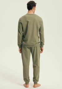 Olive green two-piece loungewear set made of soft fabric. The long-sleeve top has ribbed cuffs, and the pants have elastic ankle cuffs.
