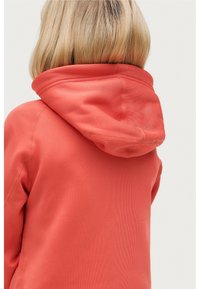 Koraalkleurige hoodie met een ronde capuchon, een gladde textuur en zichtbare stiksels. De focus ligt op het ontwerp aan de achterkant, waar de vorm van de kraag wordt getoond.