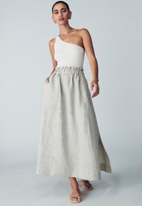 One-shoulder ribbed white top paired with a light gray linen maxi skirt featuring an elastic waistband and side slit. Flat sandals complete the look.