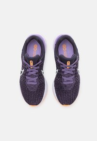 Zapatillas deportivas moradas con un upper de tejido texturizado, logotipo Swoosh blanco y acentos naranjas en la lengüeta y la suela.