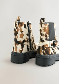 Botine cu imprimeu de leopard, cu un finisaj din blană texturată, panou lateral elastic negru, fermoar lateral și talpă groasă din cauciuc negru.