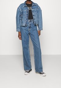 Denimjacka i ljusblått med en klassisk design, långa ärmar och knäppning med knappar. Matchas med högmidjade blå vida jeans. Svart grafisk t-shirt.