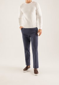 Weißer, langärmeliger Strickpullover kombiniert mit marineblauer Hose und braunen Slippern. Glatte Textur, figurbetontes Design und minimalistische Akzente.